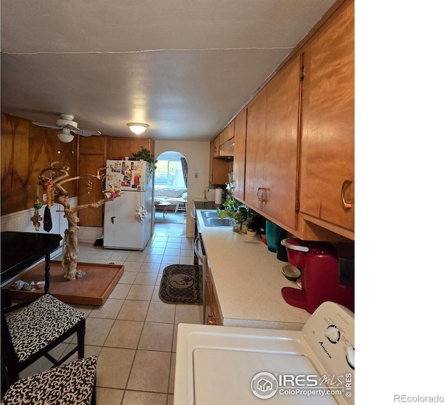 kitchen with wood walls, light tile patterned floors, ceiling fan, white fridge, and washer / clothes dryer