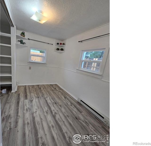 empty room featuring hardwood / wood-style floors, a textured ceiling, and a baseboard heating unit