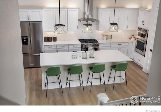 kitchen with wall chimney range hood, white cabinetry, and high quality appliances