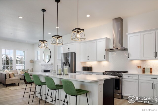 kitchen featuring wall chimney exhaust hood, stainless steel appliances, pendant lighting, and a kitchen island with sink