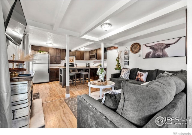 living room featuring beamed ceiling, sink, and light wood-type flooring