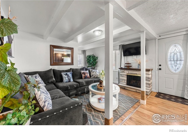 living room with a fireplace, wood-type flooring, beam ceiling, and a textured ceiling