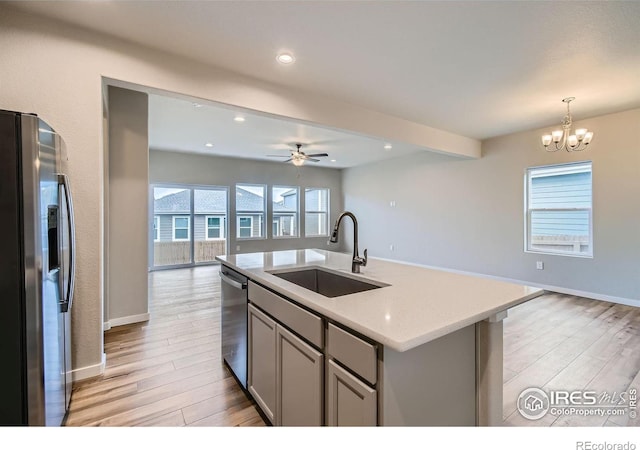 kitchen featuring sink, light stone counters, appliances with stainless steel finishes, gray cabinets, and an island with sink