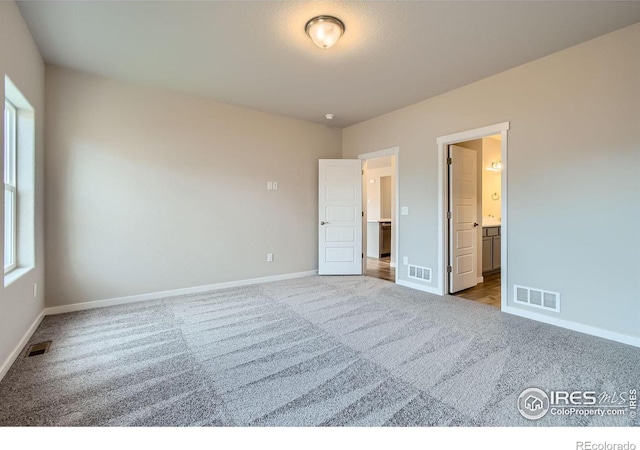 unfurnished bedroom featuring light carpet and ensuite bath