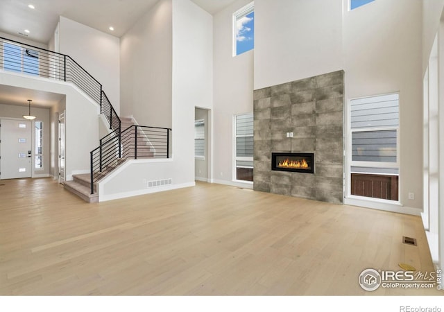 unfurnished living room with a fireplace, a high ceiling, and light hardwood / wood-style floors