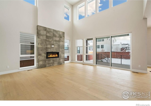 unfurnished living room featuring a tiled fireplace, light hardwood / wood-style floors, and a high ceiling