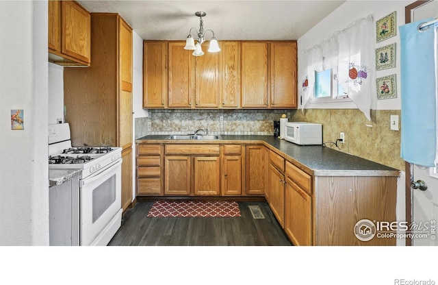 kitchen featuring dark hardwood / wood-style flooring, a chandelier, sink, backsplash, and white appliances