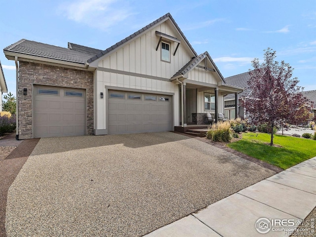 view of front of property featuring driveway, stone siding, a tile roof, an attached garage, and board and batten siding