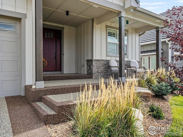 doorway to property featuring board and batten siding, covered porch, an attached garage, and stone siding