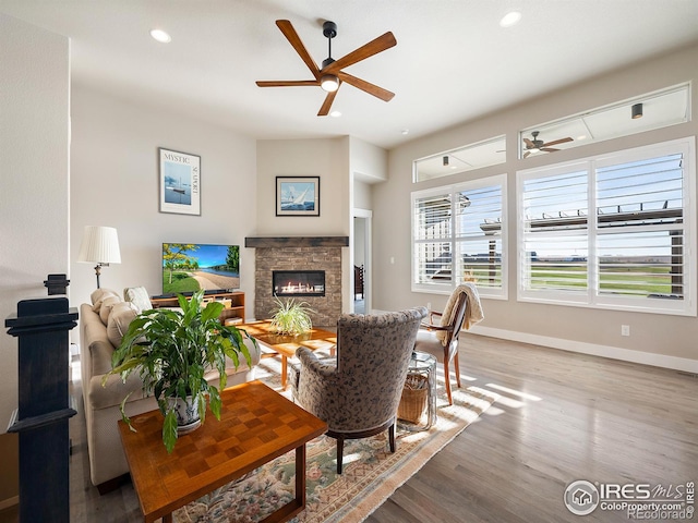 living area featuring recessed lighting, a stone fireplace, baseboards, and wood finished floors