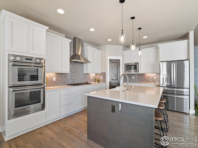 kitchen with a breakfast bar area, appliances with stainless steel finishes, white cabinetry, a sink, and wall chimney range hood