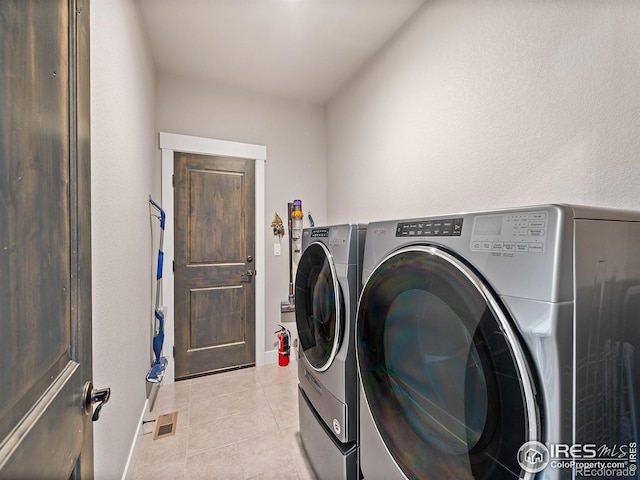 clothes washing area with washing machine and clothes dryer, light tile patterned floors, visible vents, laundry area, and baseboards