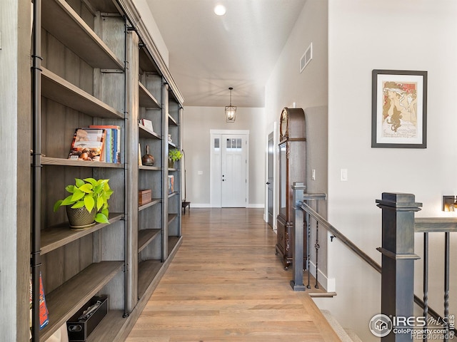 hallway with baseboards, visible vents, an upstairs landing, and wood finished floors