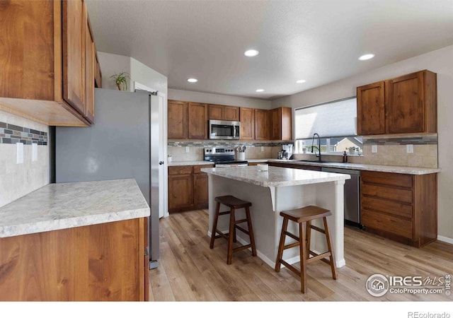 kitchen featuring sink, appliances with stainless steel finishes, a kitchen island, a kitchen bar, and light wood-type flooring