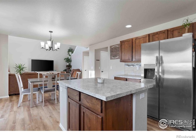 kitchen with backsplash, hanging light fixtures, light hardwood / wood-style floors, a kitchen island, and stainless steel fridge with ice dispenser