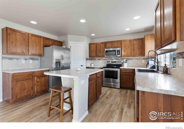 kitchen with a kitchen bar, sink, a center island, light wood-type flooring, and stainless steel appliances