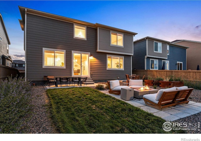 back house at dusk featuring a yard, an outdoor living space with a fire pit, and a patio area