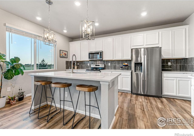 kitchen featuring pendant lighting, stainless steel appliances, white cabinets, and a center island with sink