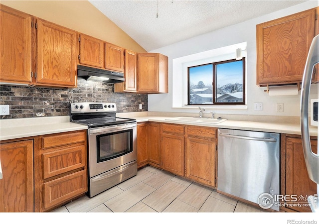 kitchen featuring lofted ceiling, decorative backsplash, a textured ceiling, sink, and appliances with stainless steel finishes