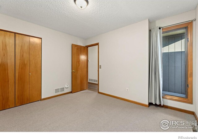 unfurnished bedroom featuring light carpet, a textured ceiling, and a closet