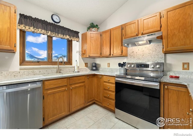 kitchen with appliances with stainless steel finishes, light tile patterned floors, light stone countertops, sink, and vaulted ceiling