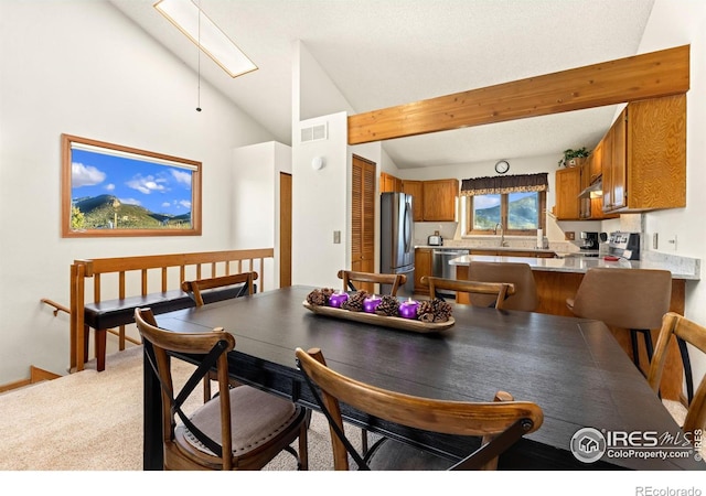 dining space featuring light carpet and vaulted ceiling with skylight