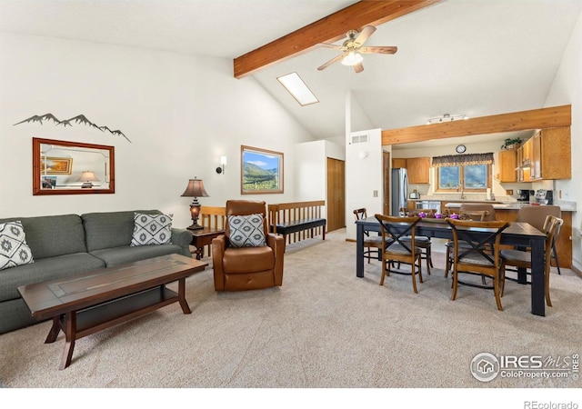 carpeted living room with ceiling fan, beam ceiling, a skylight, and high vaulted ceiling