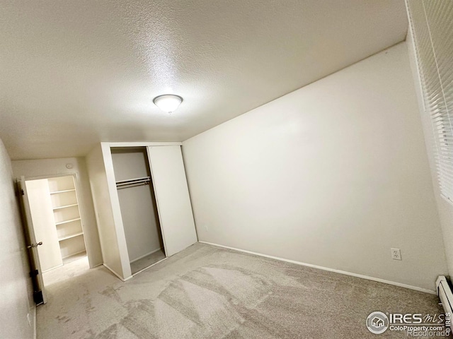 unfurnished bedroom with baseboard heating, light carpet, a closet, and a textured ceiling