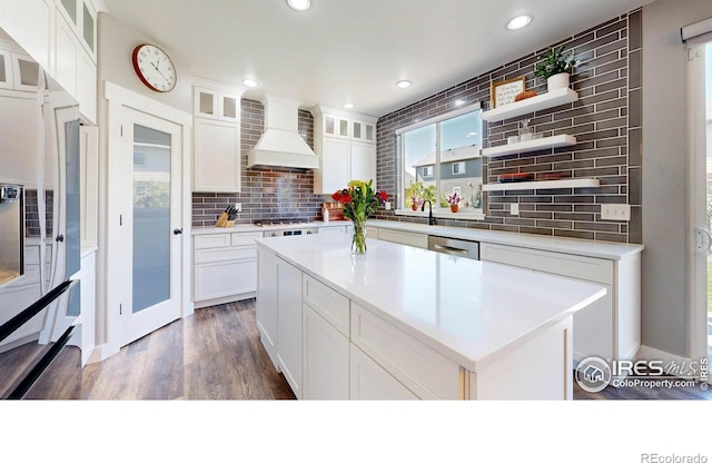 kitchen with dark wood-type flooring, white cabinets, custom exhaust hood, a kitchen island, and backsplash