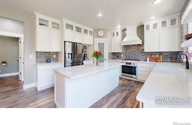 kitchen featuring sink, appliances with stainless steel finishes, a kitchen island, white cabinets, and premium range hood