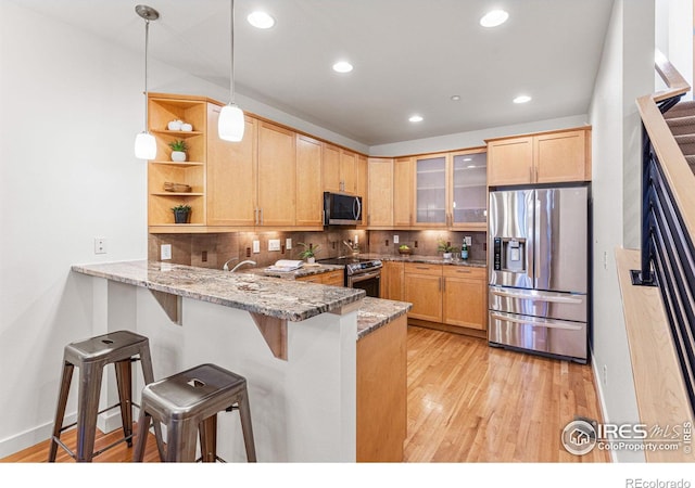 kitchen featuring kitchen peninsula, appliances with stainless steel finishes, a kitchen bar, backsplash, and light stone counters