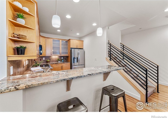 kitchen with light stone countertops, hanging light fixtures, stainless steel appliances, kitchen peninsula, and decorative backsplash