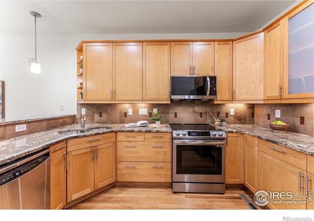 kitchen with light stone countertops, sink, stainless steel appliances, light hardwood / wood-style floors, and decorative light fixtures