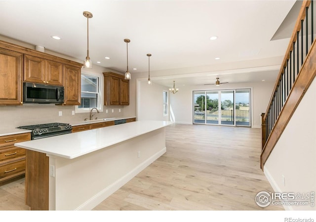 kitchen with sink, backsplash, a kitchen island, gas range, and decorative light fixtures