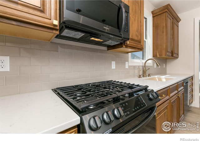 kitchen featuring gas range oven, sink, decorative backsplash, and light hardwood / wood-style flooring