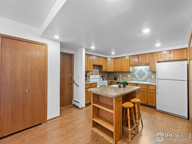 kitchen featuring a baseboard radiator, a kitchen breakfast bar, a center island, white appliances, and light hardwood / wood-style flooring