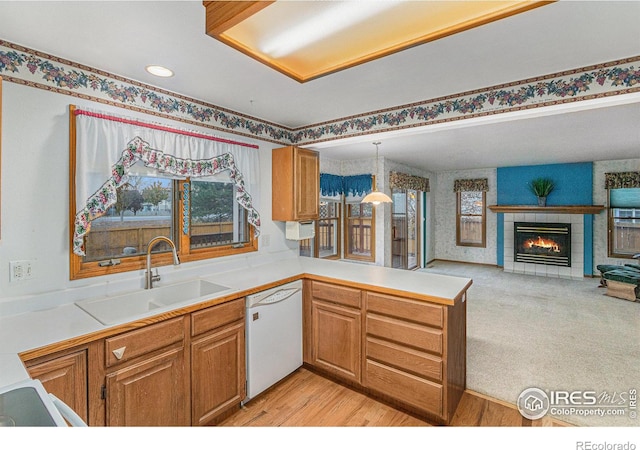 kitchen featuring dishwasher, kitchen peninsula, sink, pendant lighting, and light hardwood / wood-style flooring