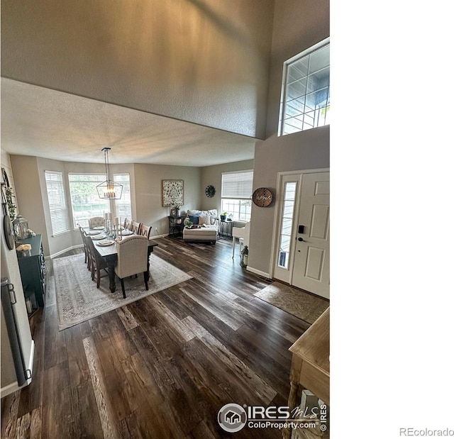 foyer entrance featuring dark wood-type flooring, a textured ceiling, a healthy amount of sunlight, and a towering ceiling