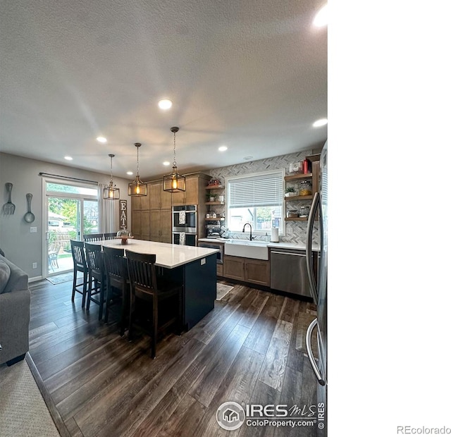 kitchen with stainless steel appliances, dark hardwood / wood-style flooring, a center island, hanging light fixtures, and a breakfast bar