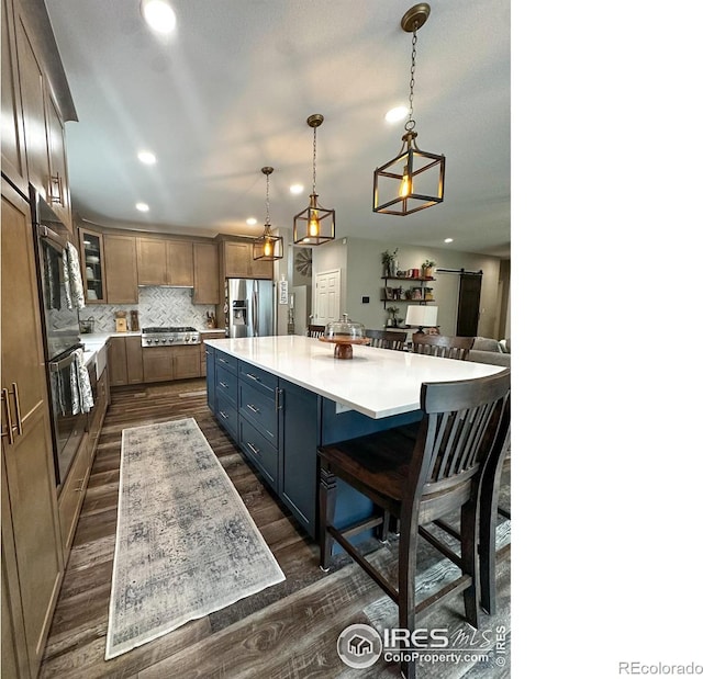 kitchen with appliances with stainless steel finishes, a large island, a barn door, dark hardwood / wood-style flooring, and pendant lighting