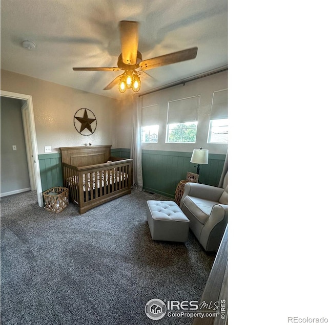 carpeted bedroom with a textured ceiling, a nursery area, and ceiling fan