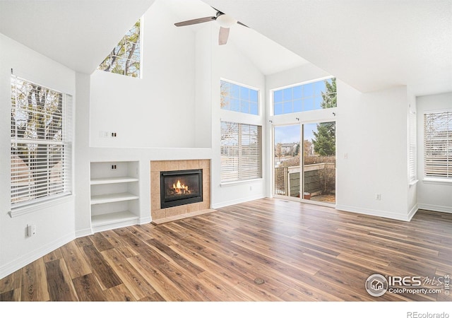 unfurnished living room featuring ceiling fan, high vaulted ceiling, built in features, a tile fireplace, and dark hardwood / wood-style flooring