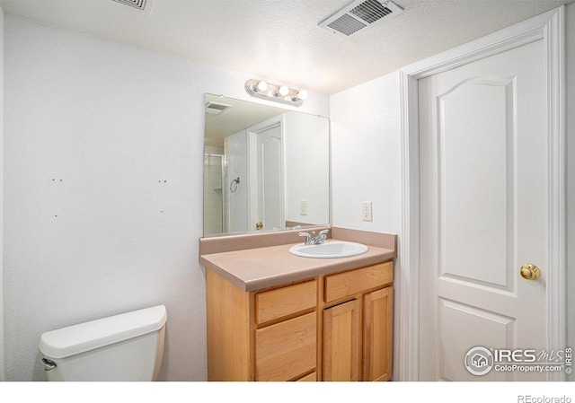 bathroom with vanity, a textured ceiling, toilet, and a tile shower