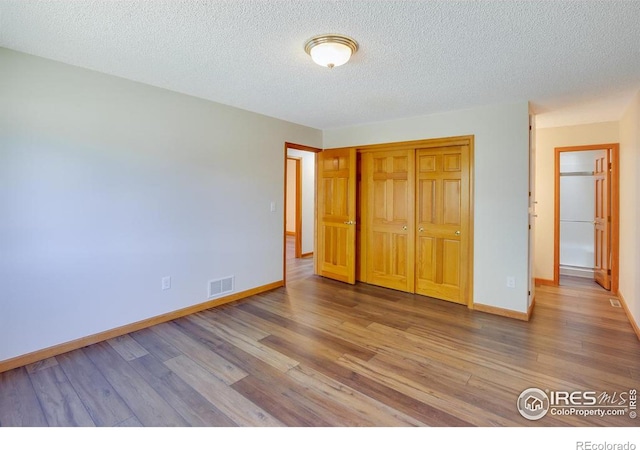 unfurnished bedroom with wood-type flooring, a closet, and a textured ceiling