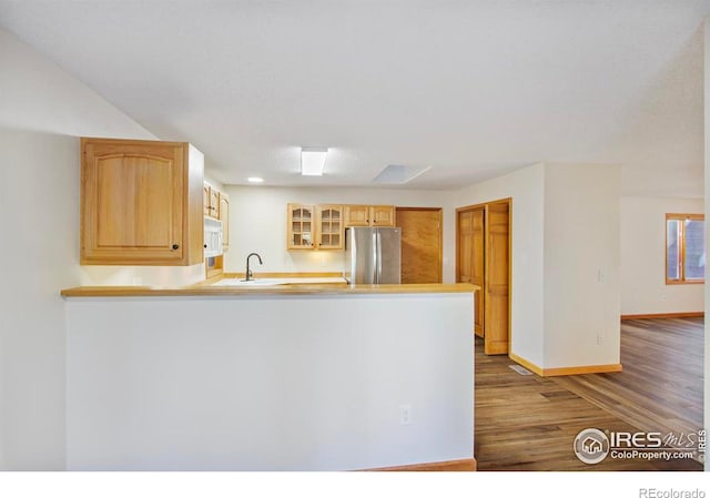 kitchen with light brown cabinetry, wood-type flooring, sink, stainless steel fridge, and kitchen peninsula