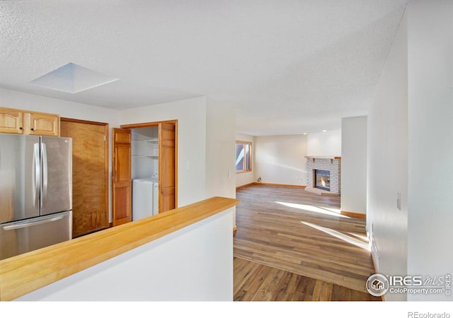 kitchen with hardwood / wood-style flooring, stainless steel fridge, a textured ceiling, a brick fireplace, and light brown cabinets