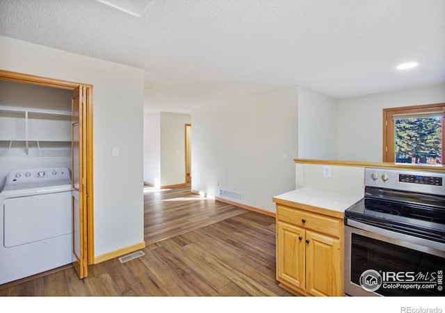 kitchen featuring washer / clothes dryer, wood-type flooring, stainless steel range with electric stovetop, light brown cabinets, and a textured ceiling