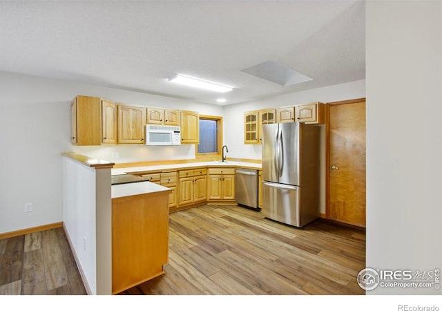 kitchen with light brown cabinetry, sink, a textured ceiling, stainless steel appliances, and light hardwood / wood-style floors