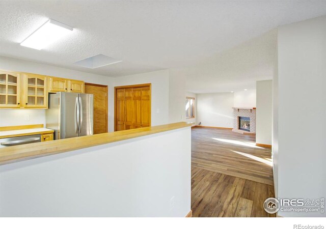 kitchen with appliances with stainless steel finishes, a fireplace, a textured ceiling, dark hardwood / wood-style flooring, and light brown cabinets