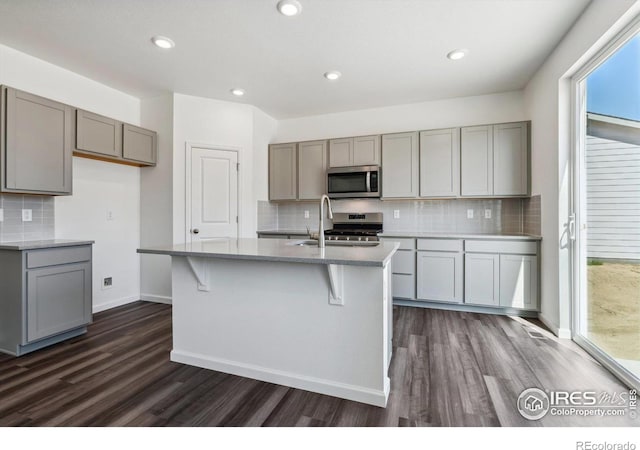 kitchen with dark wood-type flooring, gray cabinetry, appliances with stainless steel finishes, and an island with sink